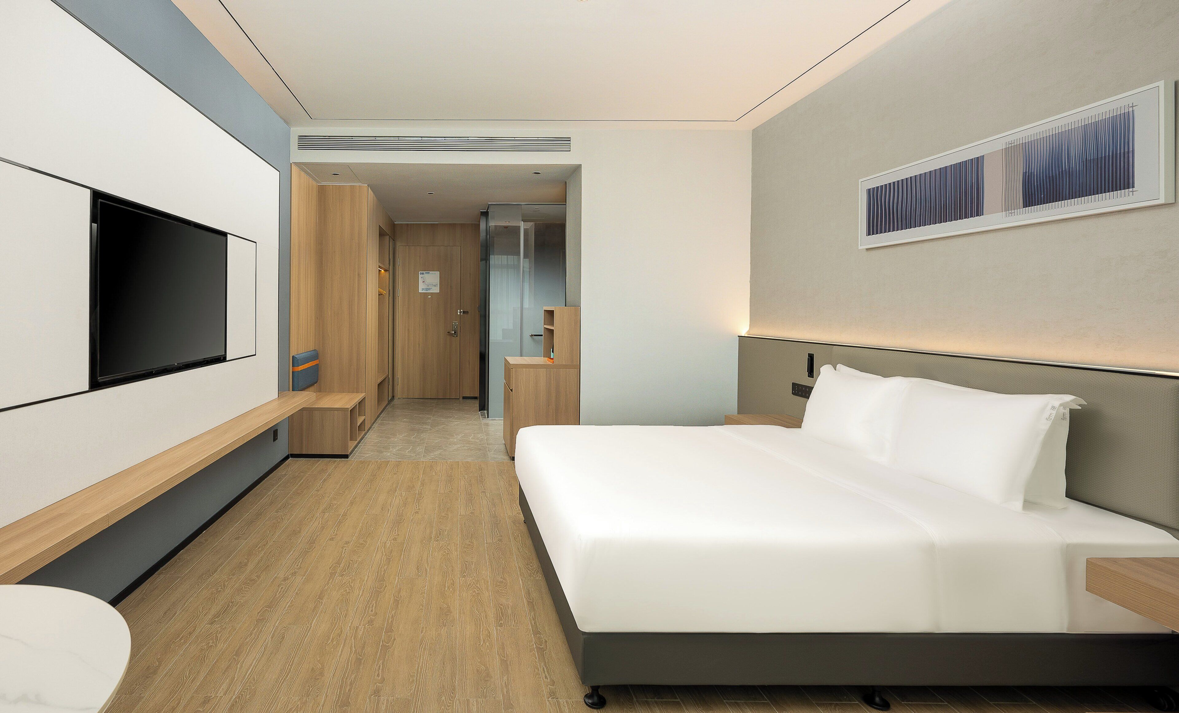 A modern hotel room with a large bed, a flat-screen TV, a desk, and a wardrobe.