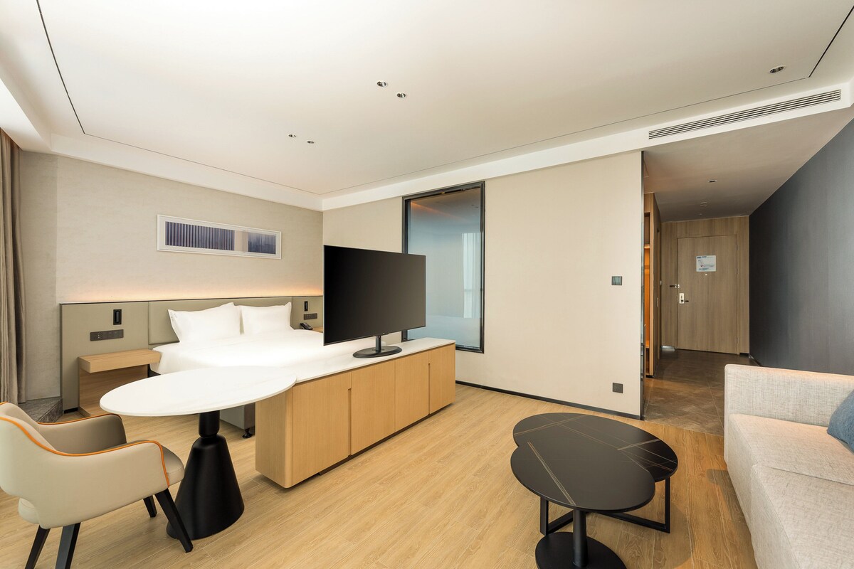 A modern hotel room with a bed, a TV, a desk, and a sofa.