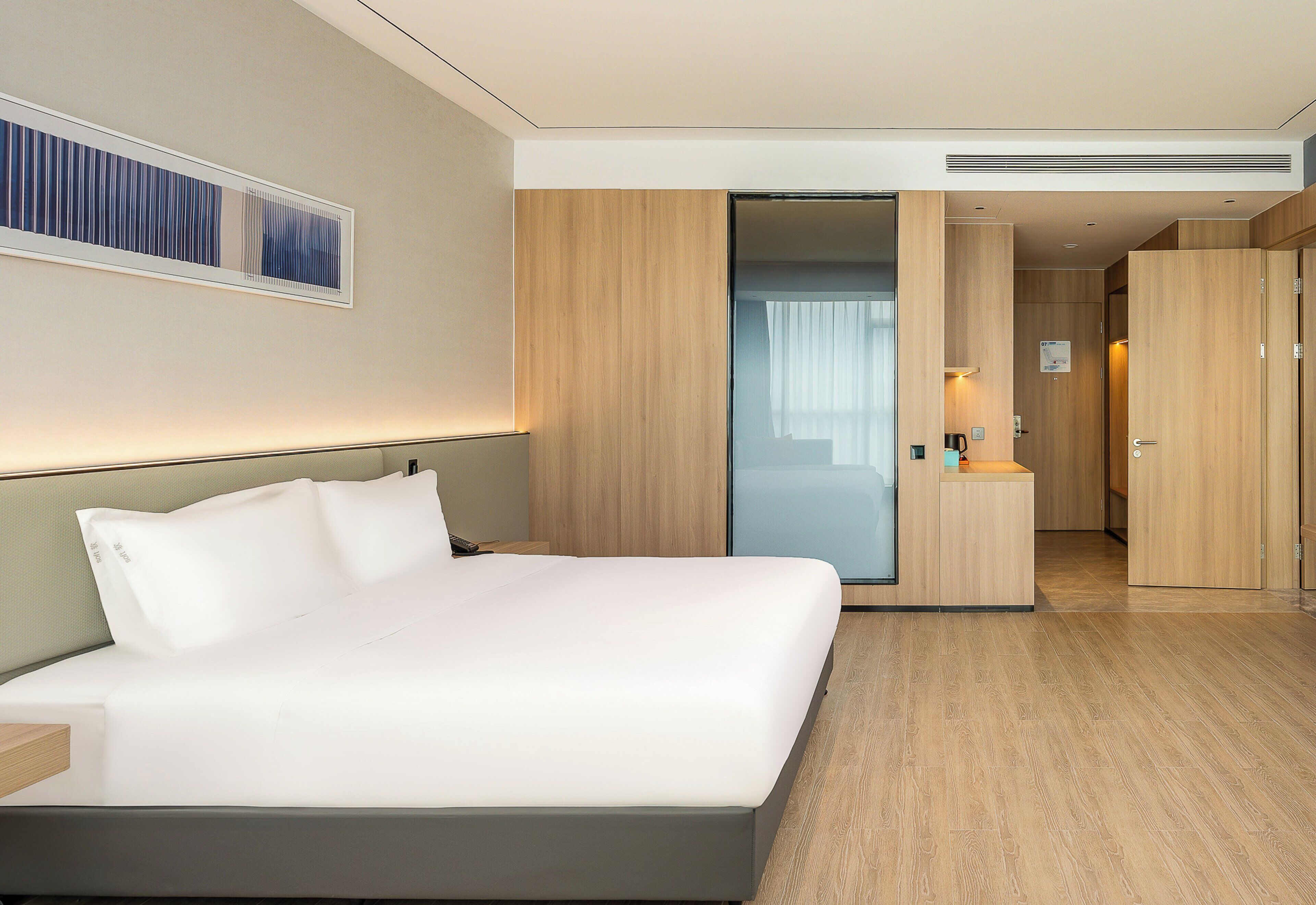 A modern hotel room with a large bed, wooden paneling, a desk, and a glass partition.