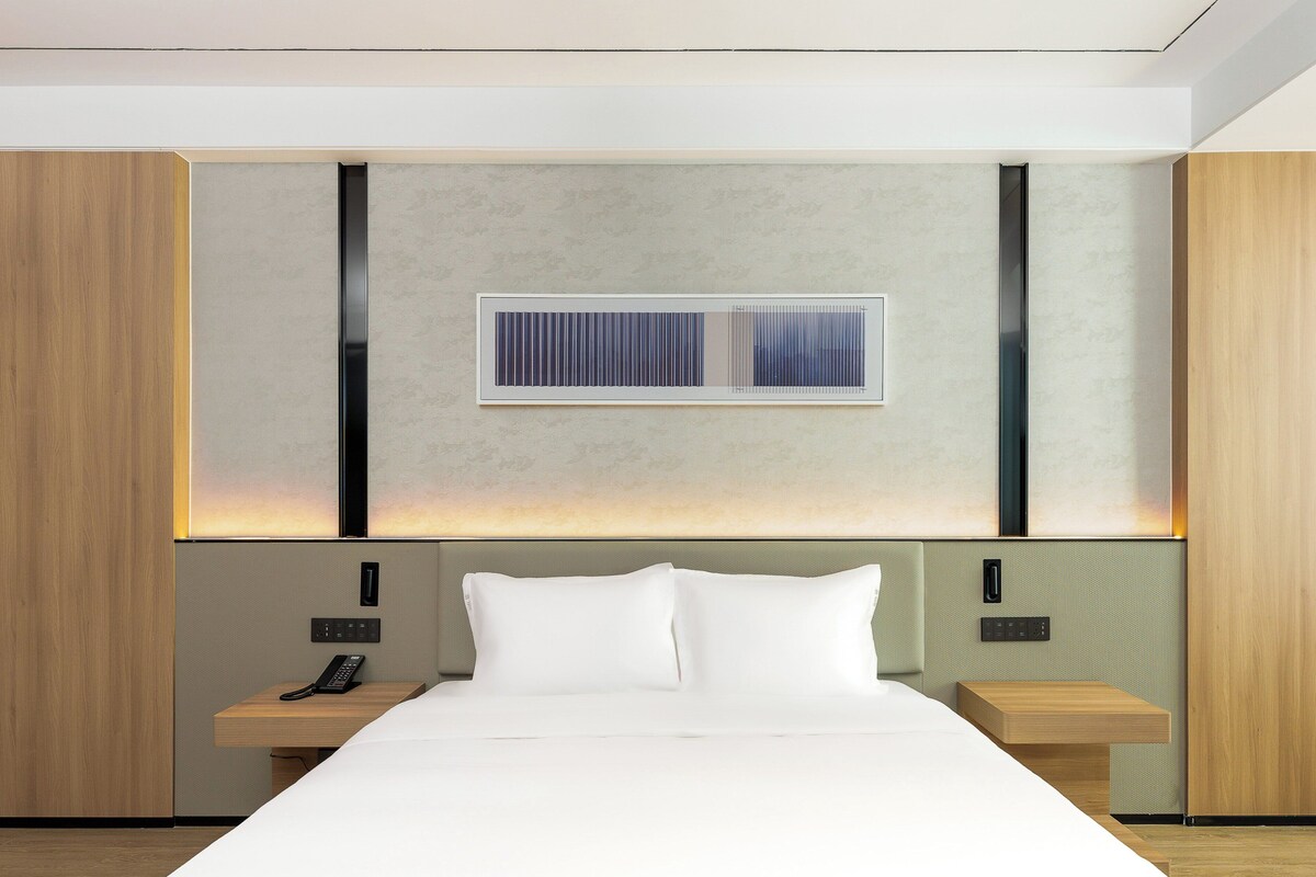 A modern hotel room with a large bed, bedside tables, a built-in telephone, and a wall-mounted light fixture.
