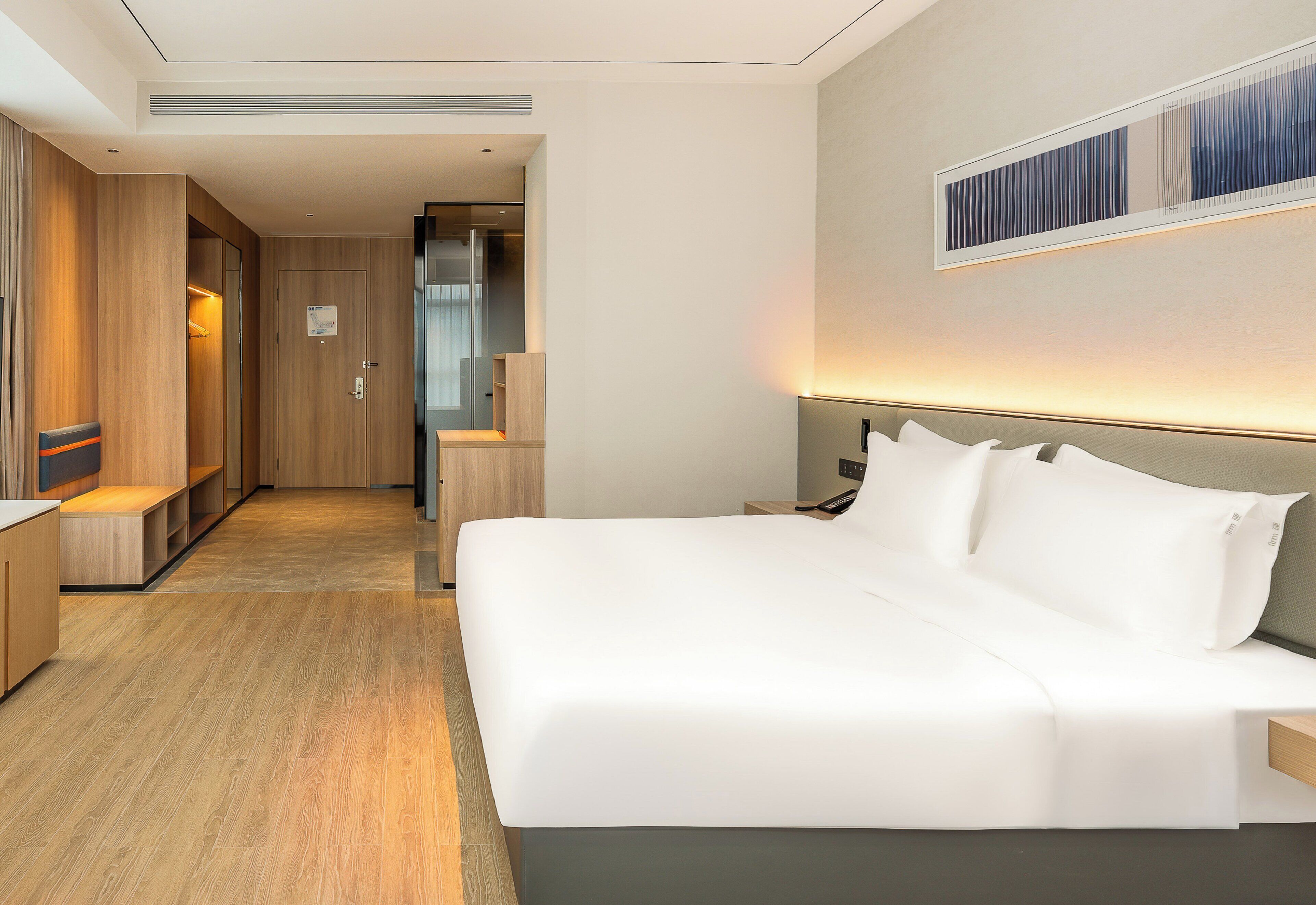 A hotel room with a large bed, wooden flooring, a desk, and a mirror on the wall.