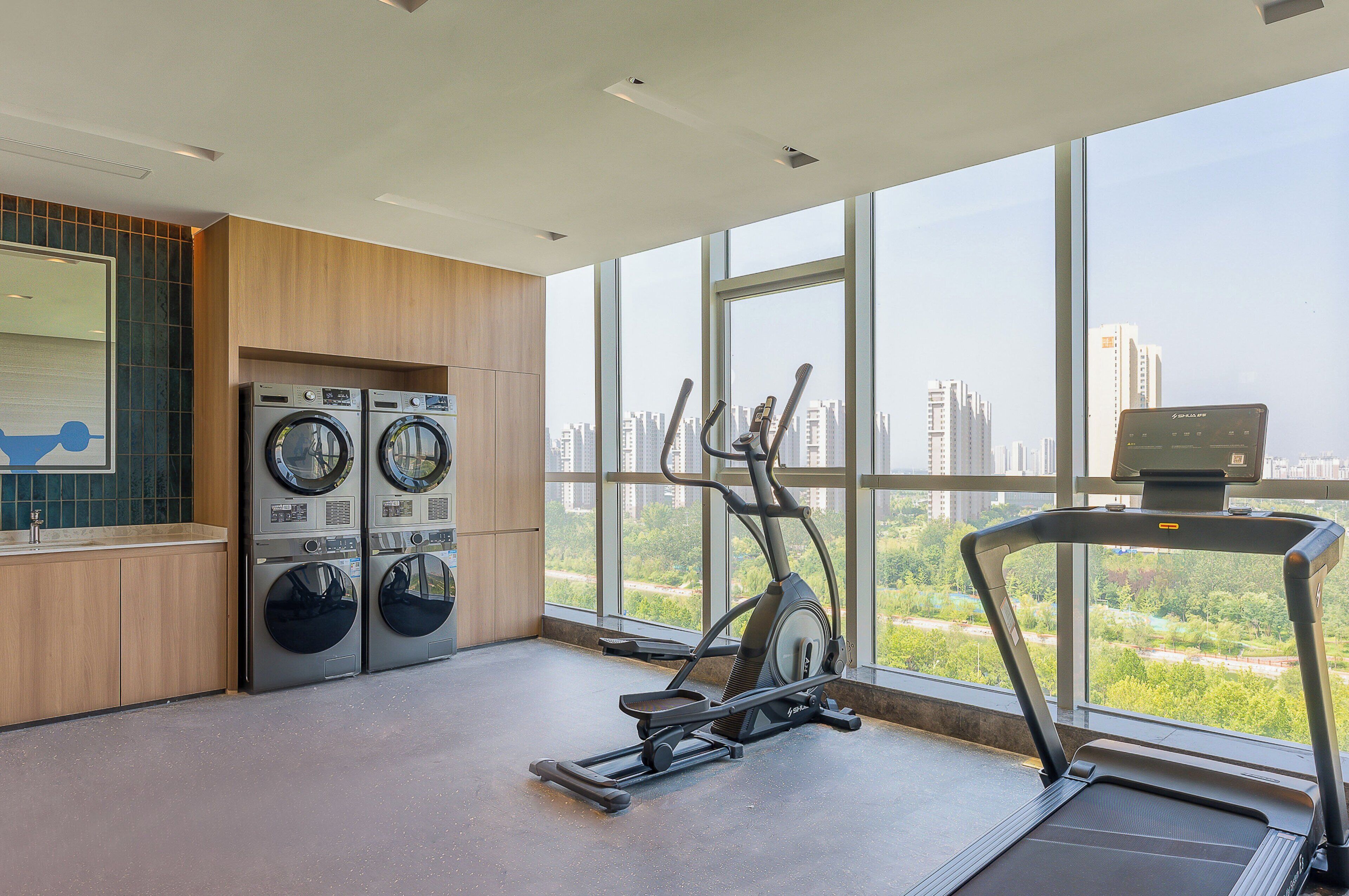 Une salle de sport équipée d’un tapis de course, d’un vélo elliptique et de deux machines à laver fixées au mur.
