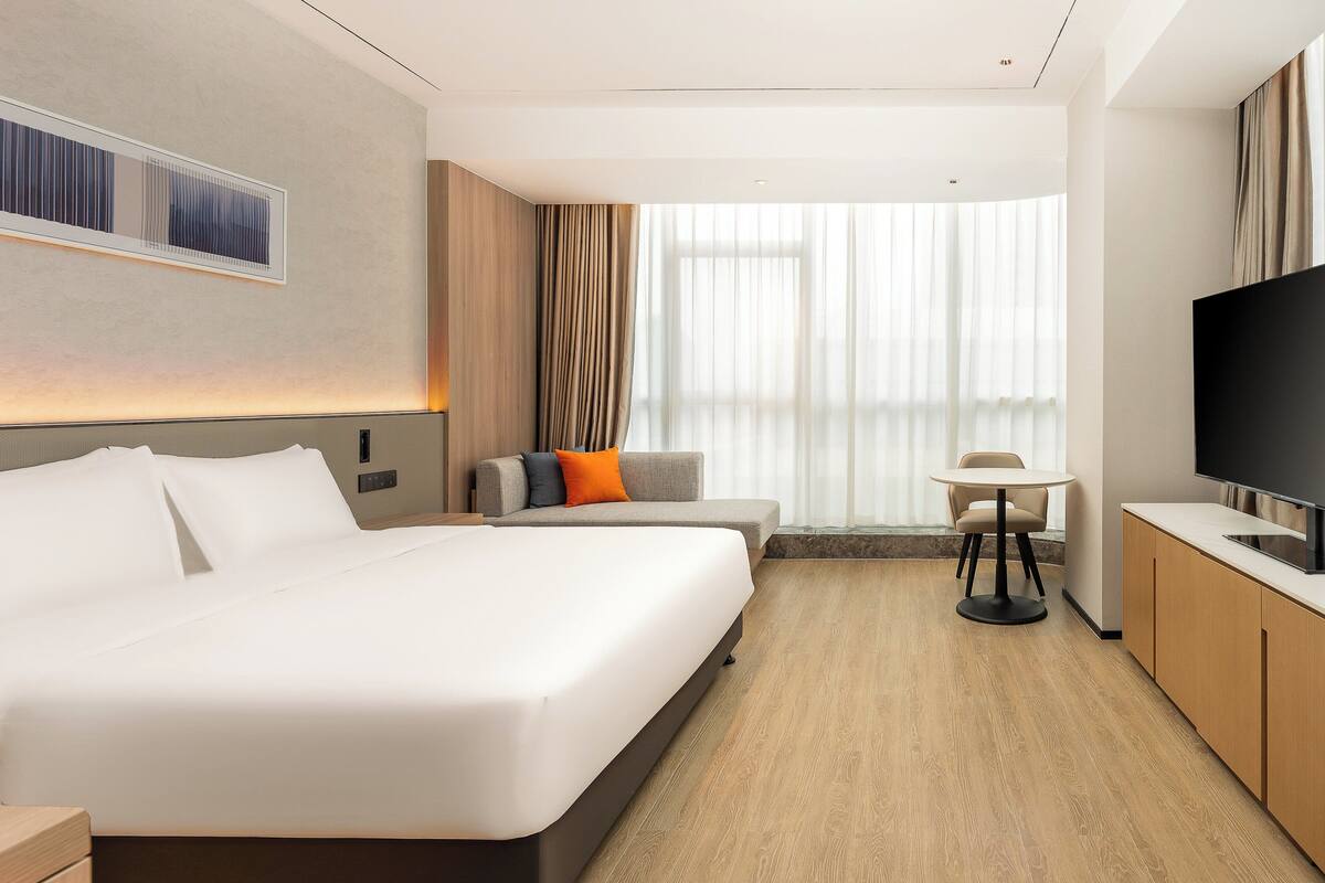 A modern hotel room with a large bed, a sofa, a small table, and a TV.