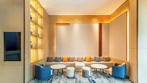 A modern lounge area with a sofa, chairs, and tables, featuring a patterned carpet and recessed lighting.