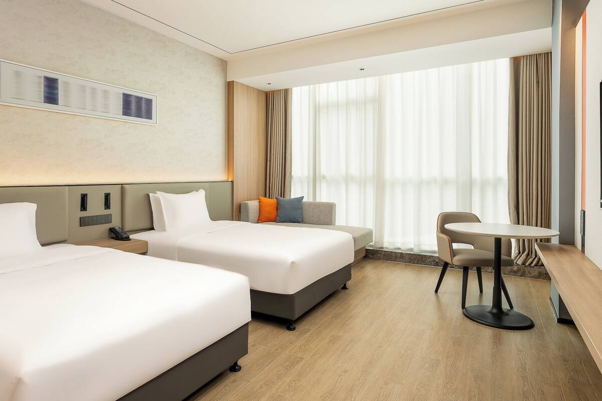 A hotel room with two beds, a small table, a chair, and a TV.