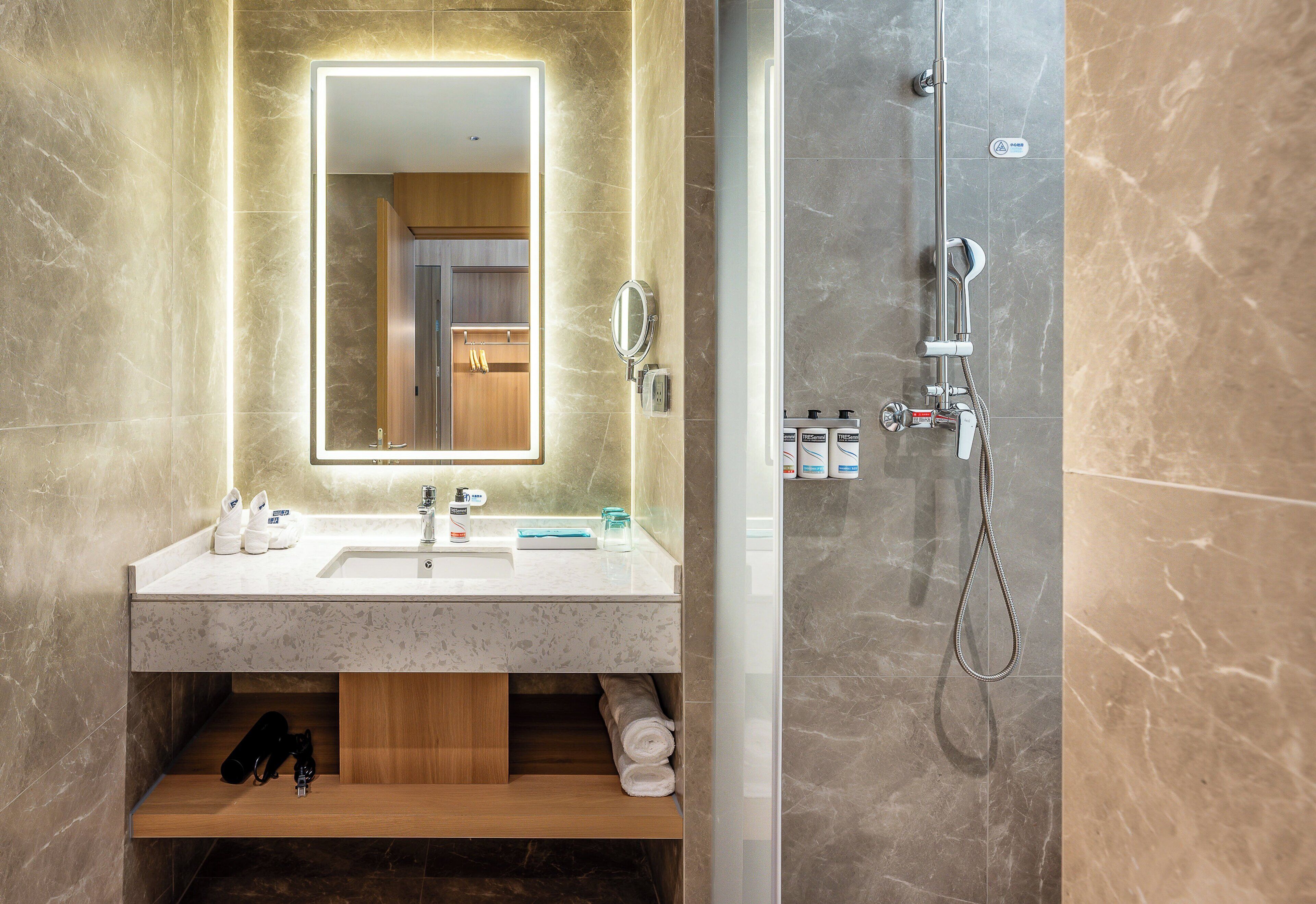 Un baño moderno con tocador de mármol, un espejo grande, ducha con cabezal de ducha manual y un perchero para toallas.