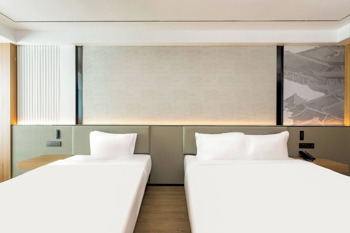 A hotel room with two beds, a large wall-mounted artwork, and a wooden floor.