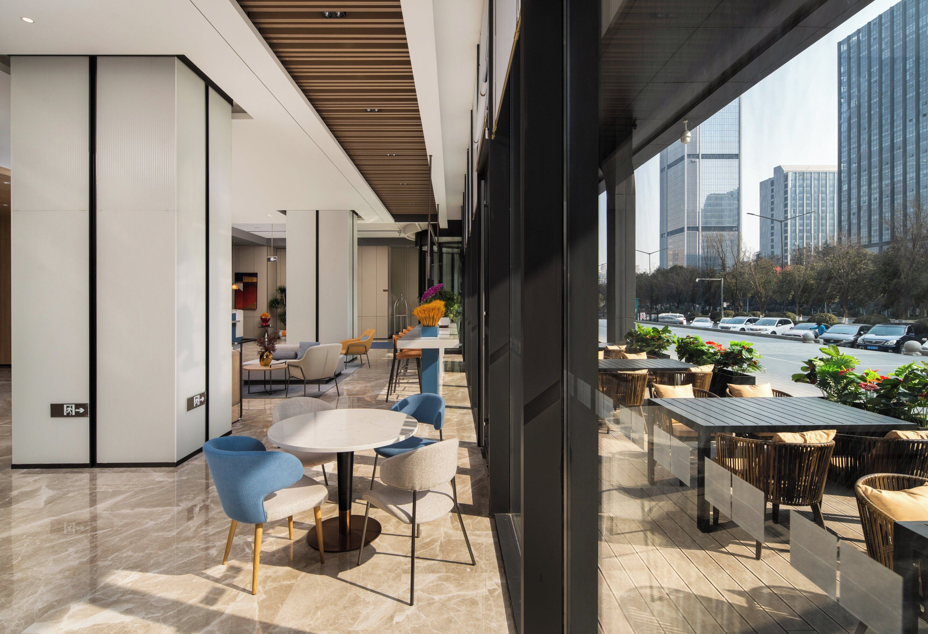 A modern indoor seating area with tables and chairs, a glass wall offering a view of the cityscape and parked cars.