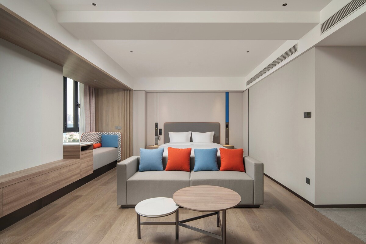 A modern hotel room with a large bed, a sofa, and a round table.