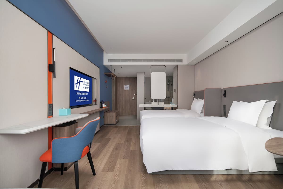 A hotel room with a bed, a desk with a chair, a TV, and a bathroom.