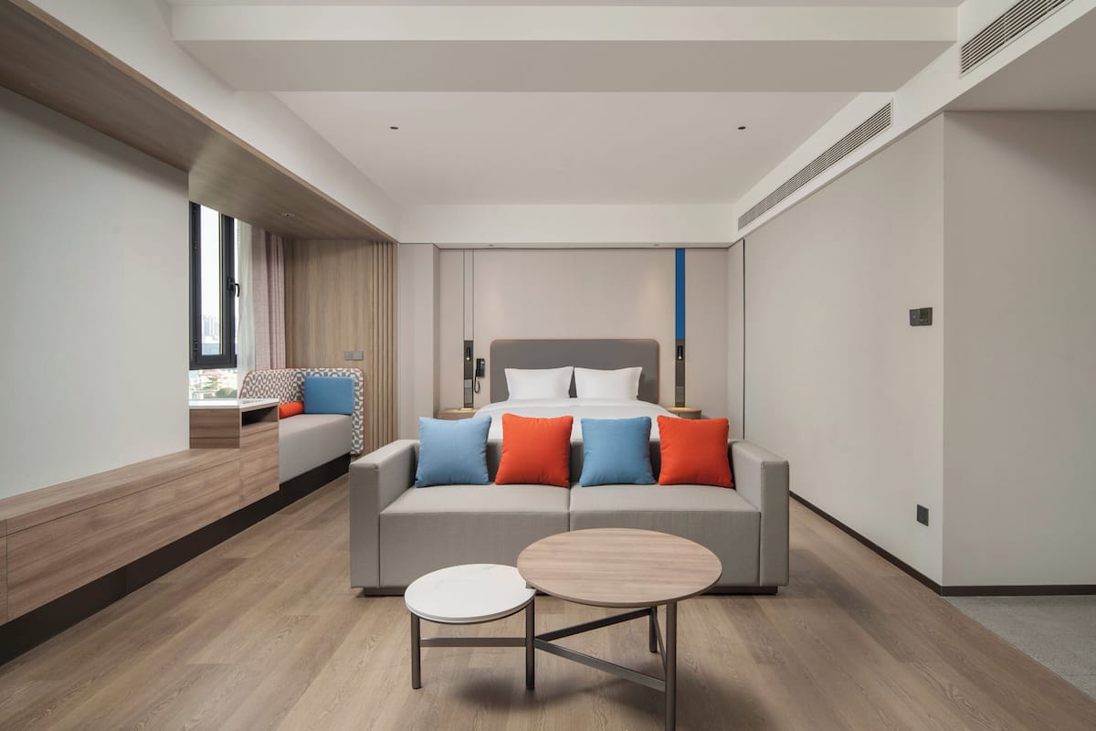 A modern hotel room with a large bed, a sofa, and a round table.