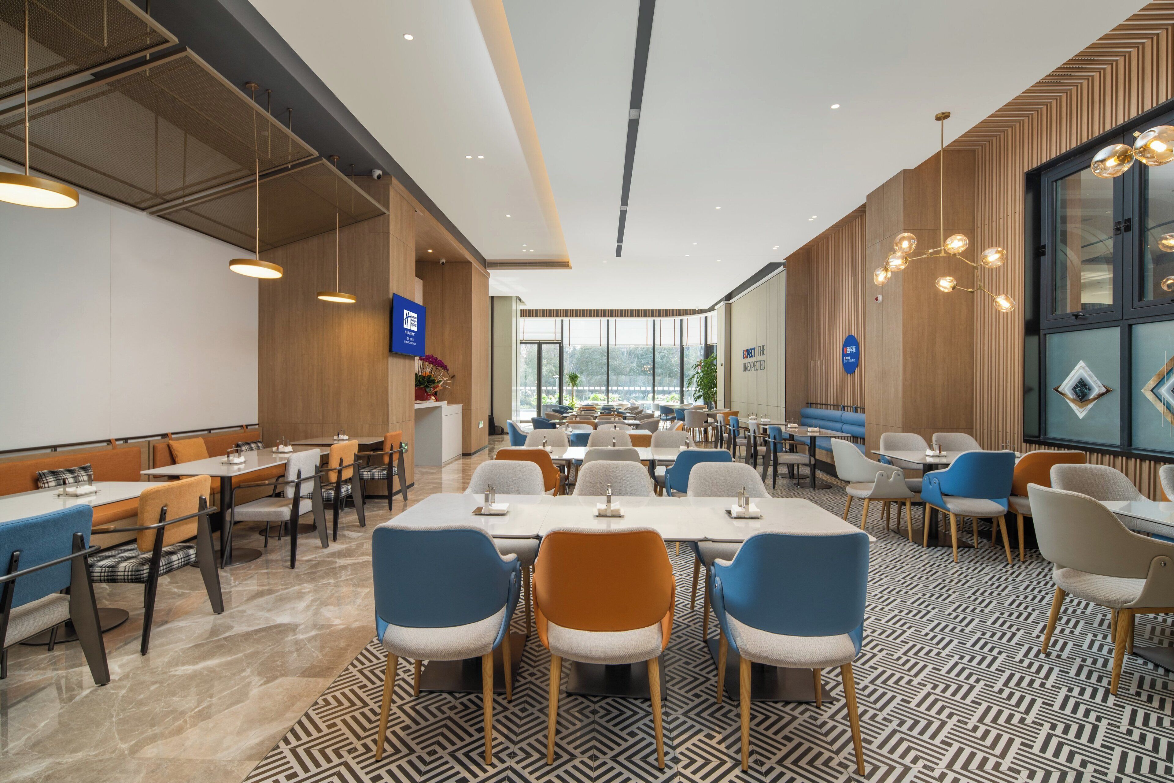 A modern dining area with multiple tables and chairs, a patterned floor, and a view of the outdoors through large windows.