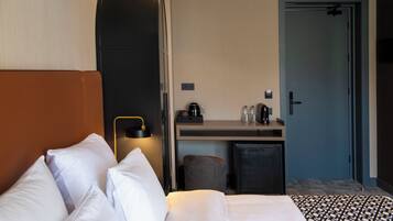 Quarto de hotel com cama, escrivaninha, cafeteira e porta.