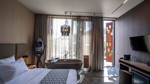 Quarto de hotel moderno com uma cama grande, banheira, televisão e vista para o exterior.