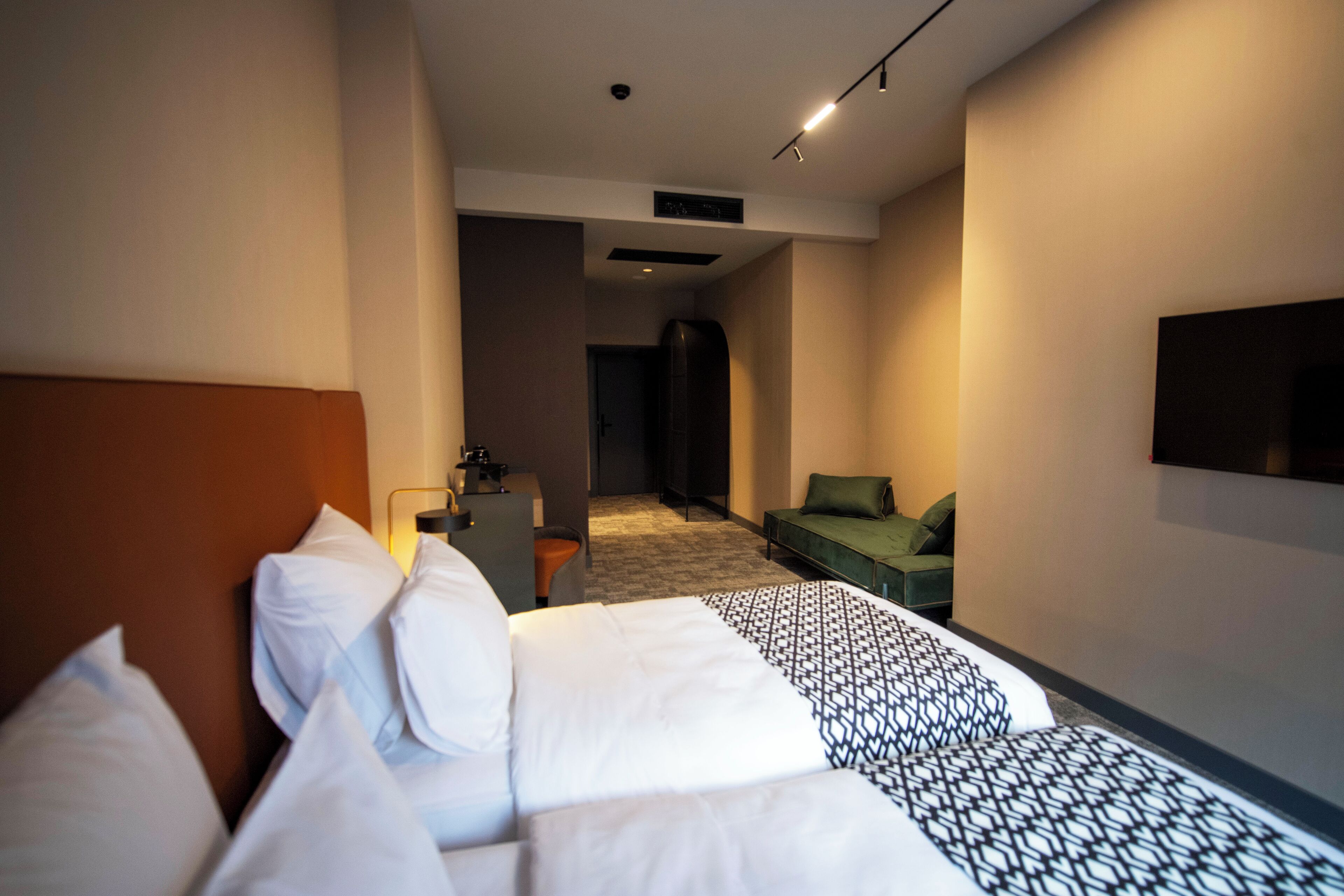 A hotel room with a large bed, a desk, a green sofa, and a TV mounted on the wall.