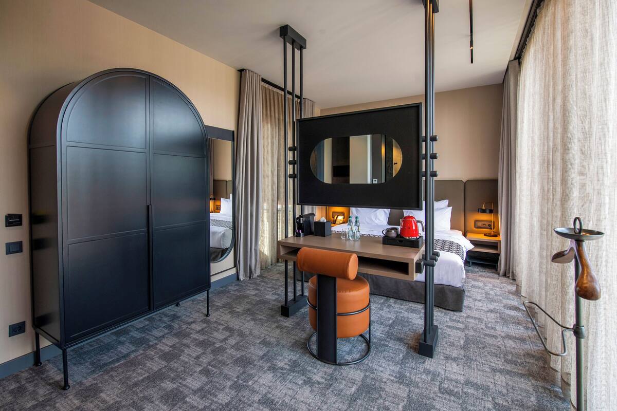 Habitación de hotel con un armario arqueado grande, un escritorio con silla, una cama y un espejo grande.