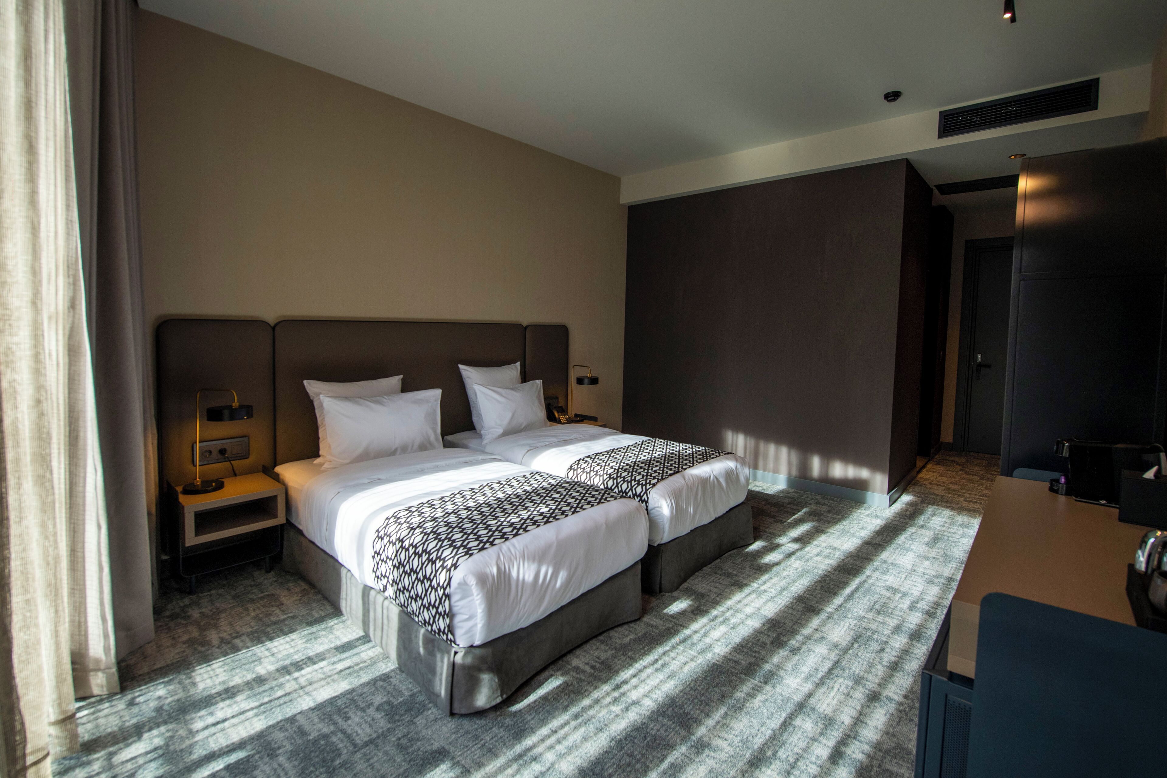 Quarto de hotel com duas camas, uma escrivaninha e uma mesa de cabeceira.