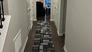 A hallway with a patterned rug, white walls, and a door leading to a room.