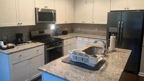 A modern kitchen with white cabinets, a stainless steel refrigerator, a microwave, and a granite countertop.