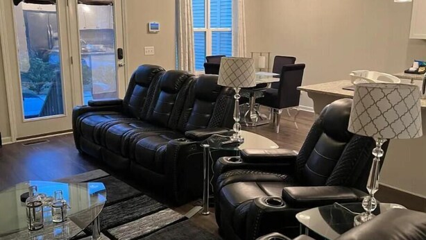 A modern living room with a black leather sofa, a glass coffee table, and two lamps.