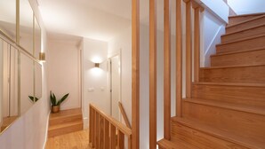 A wooden staircase with a handrail, a potted plant, and a light fixture on the wall.