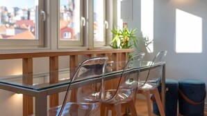 A modern interior with a glass table and chairs, a potted plant, and a view of buildings through large windows.