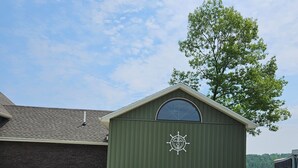 A green shed with a circular emblem, a paved driveway, and a grassy lawn.