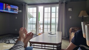 A living room with a television, a table, and a view of a body of water through large windows.