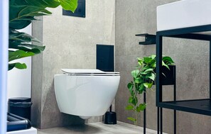 Une salle de bain moderne avec des toilettes, une étagère noire et une plante en pot.