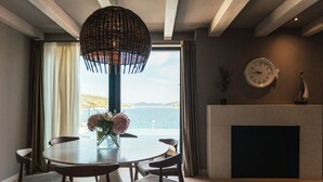Un comedor con una mesa redonda y sillas, un florero con flores, un reloj en la pared y vistas al mar.