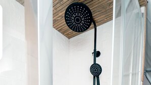 A shower with a black handheld showerhead and a rain shower attachment.
