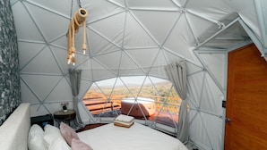 A geodesic dome room with a bed, a small table, and a view of the outdoors.