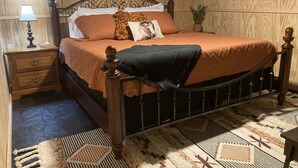 A wooden-paneled bedroom with a bed, nightstand, lamp, and a potted plant.