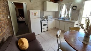 Eine kompakte Küche mit Kühlschrank, Herd, Mikrowelle und Spüle. Es gibt einen Essbereich mit Tisch und Stühlen sowie ein Wohnzimmer mit einer Couch.