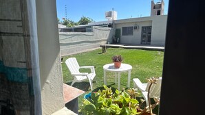 Blick aus einem Fenster auf eine Terrasse mit einem weißen Stuhl, einem kleinen runden Tisch und einem Blumentopf.
