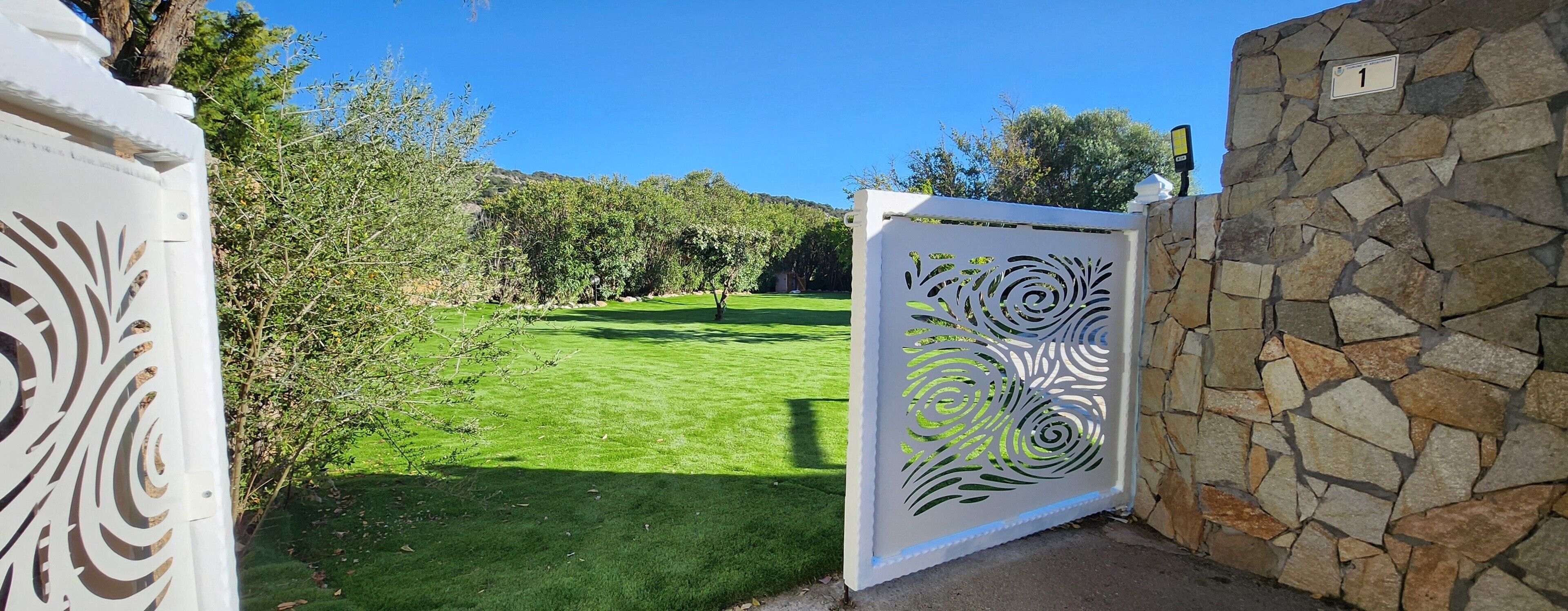 Una entrada con reja y un diseño metálico decorativo, un muro de piedra y un césped bien cuidado.