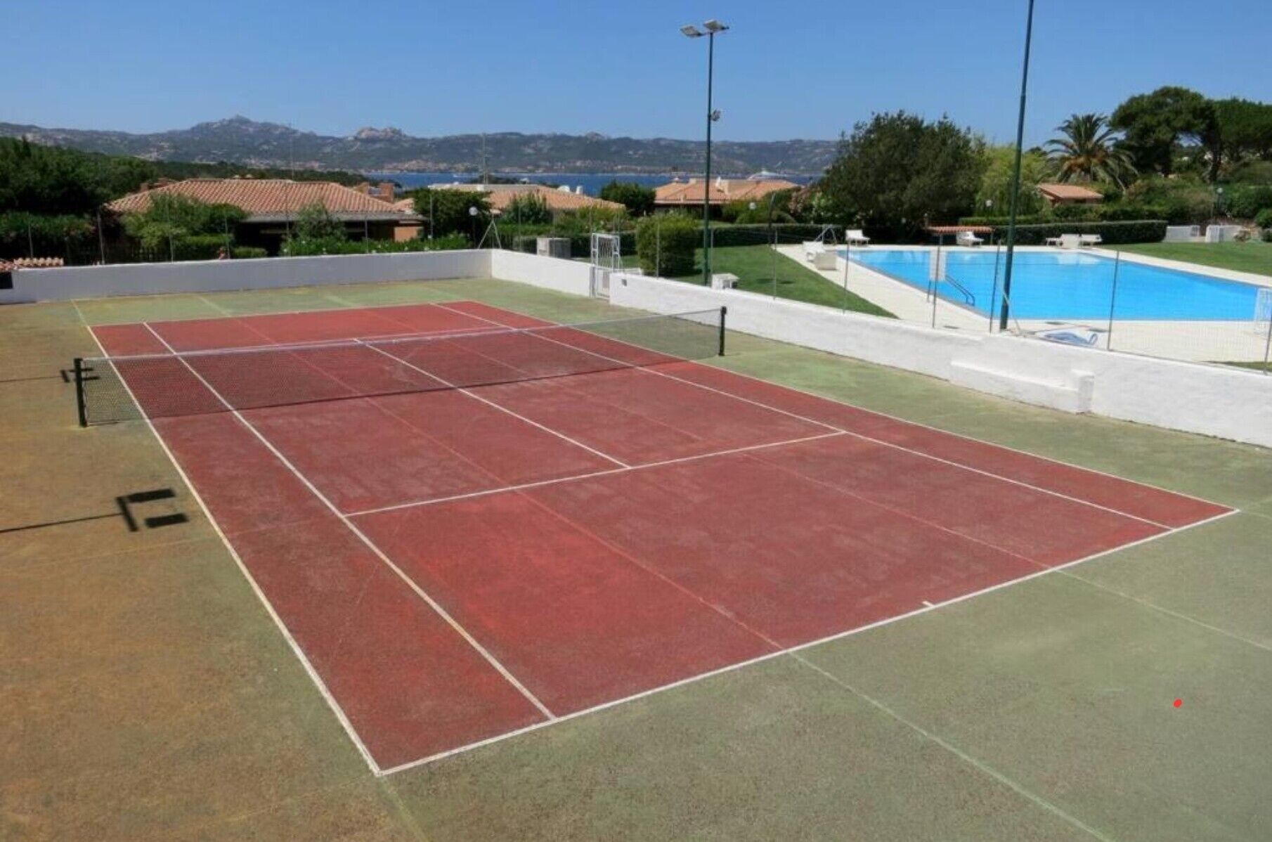Una cancha de tenis con piscina y montañas al fondo.