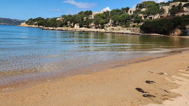 A beach with clear water, pebbly shore, and buildings in the background. - Villa 'Alba Baja Sardinia' with Sea View, Shared Pool, and Wi-Fi (Baja Sardinia Arzachena)