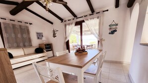 A dining area with a wooden table and white chairs, a sofa, and a television in the background. - Villa 'Alba Baja Sardinia' with Sea View, Shared Pool, and Wi-Fi (Baja Sardinia Arzachena)