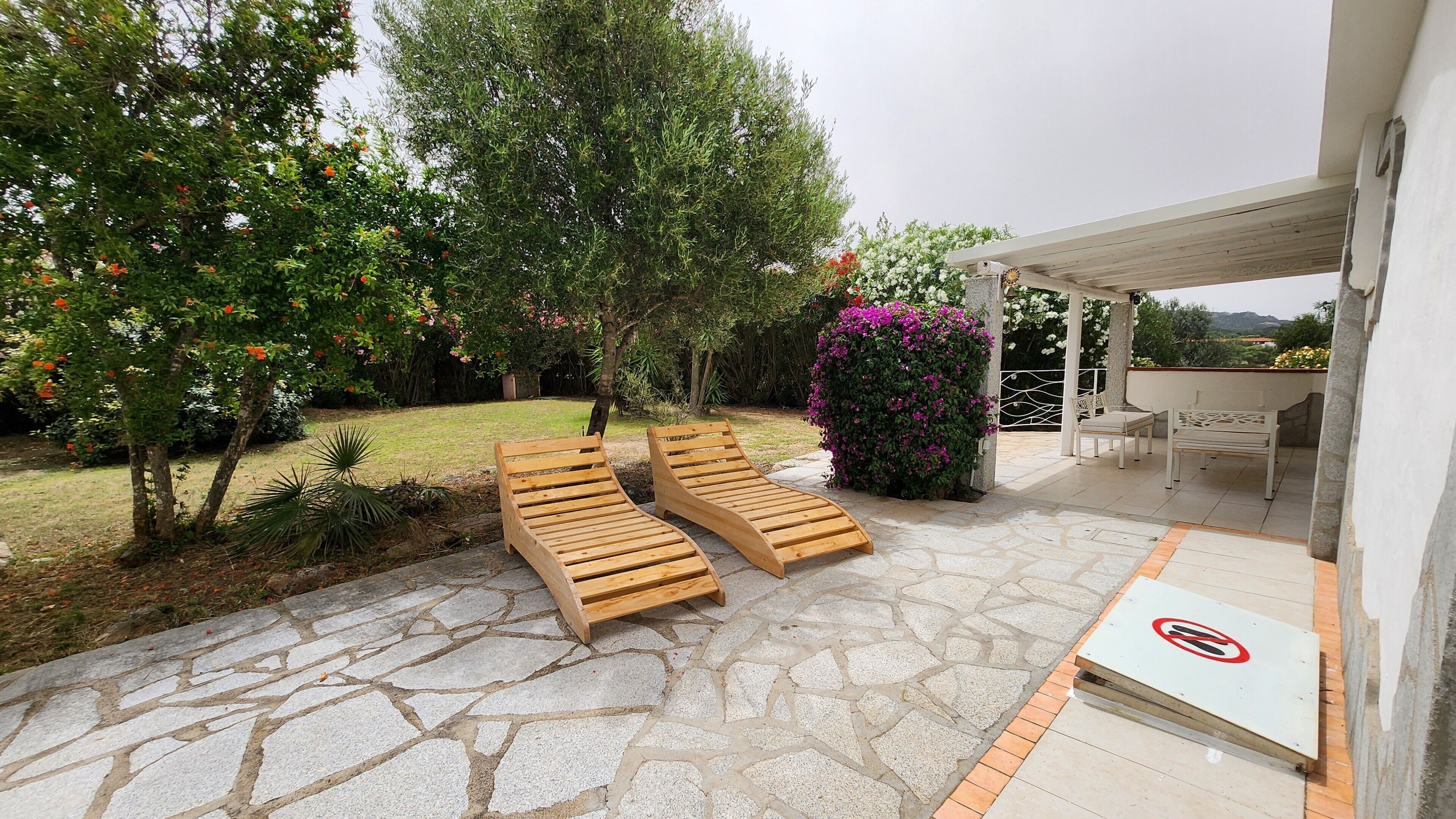 Une terrasse avec deux chaises longues en bois, un espace salon couvert et un sol carrelé en pierre.