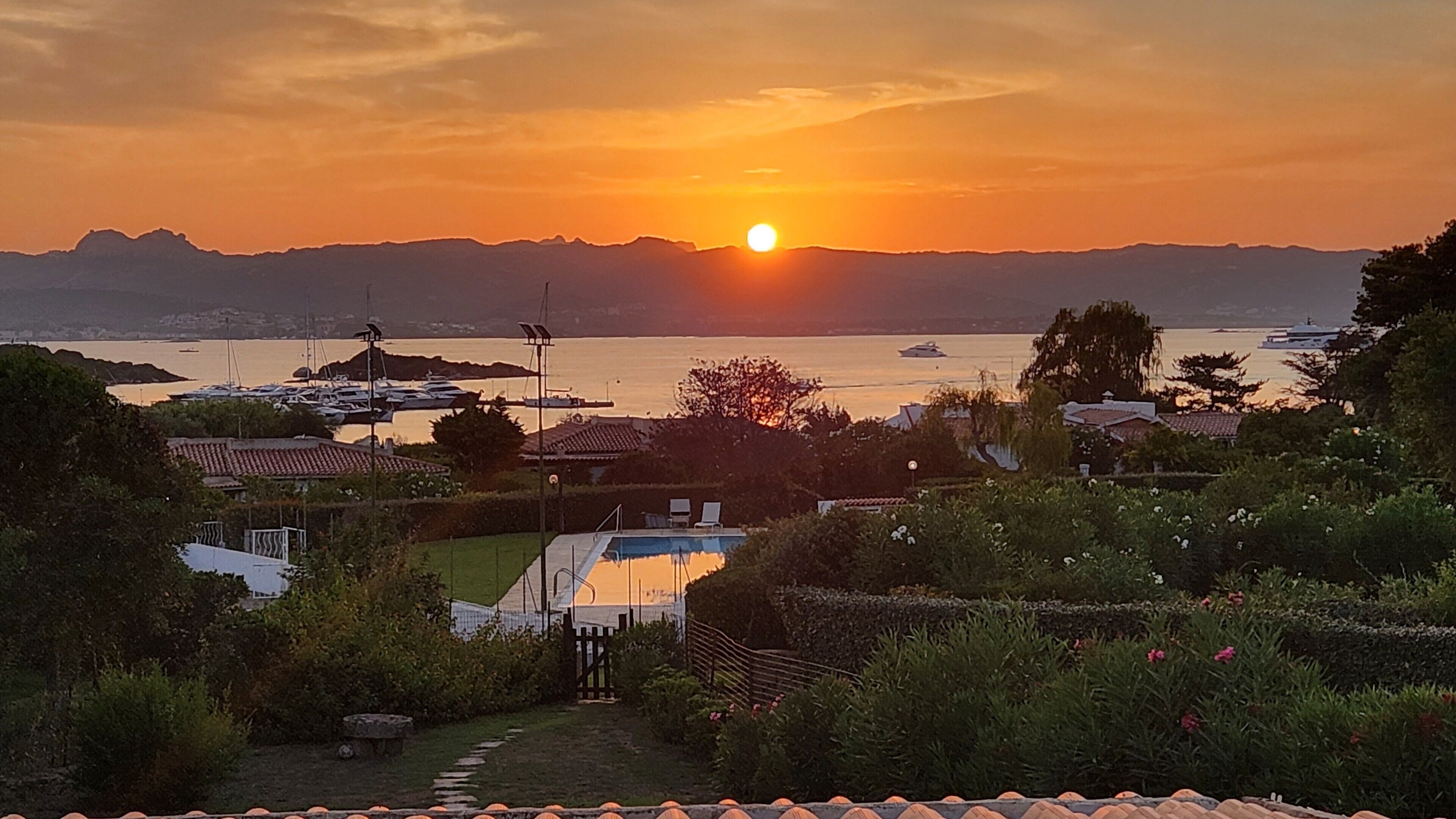 Ein Sonnenuntergang über einem Yachthafen mit Booten, einem Schwimmbad und Wohnhäusern.