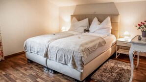 Ein ordentlich bezogenes Bett mit Kopfteil, ein Nachttisch mit Lampe und ein kleiner Blumentopf.