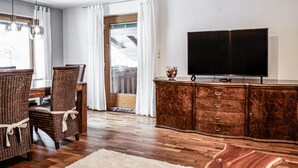 Ein Wohnzimmer mit Holzboden, Korbmöbeln, einem Flachbildfernseher und Blick auf einen Balkon.