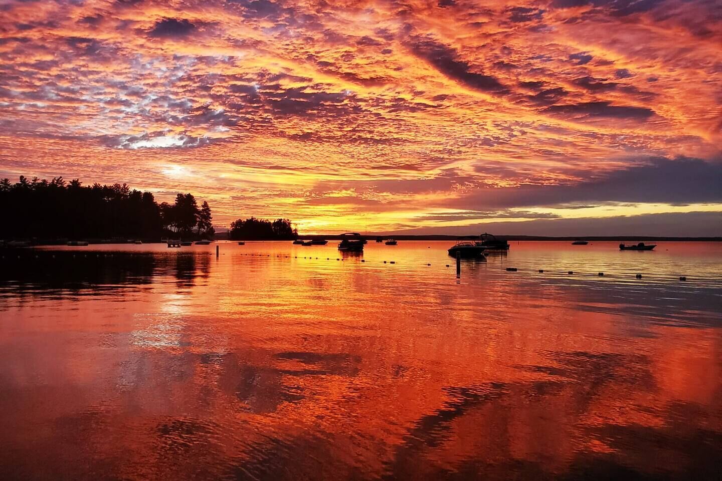 Un lago tranquilo al atardecer con barcos y una orilla arbolada.