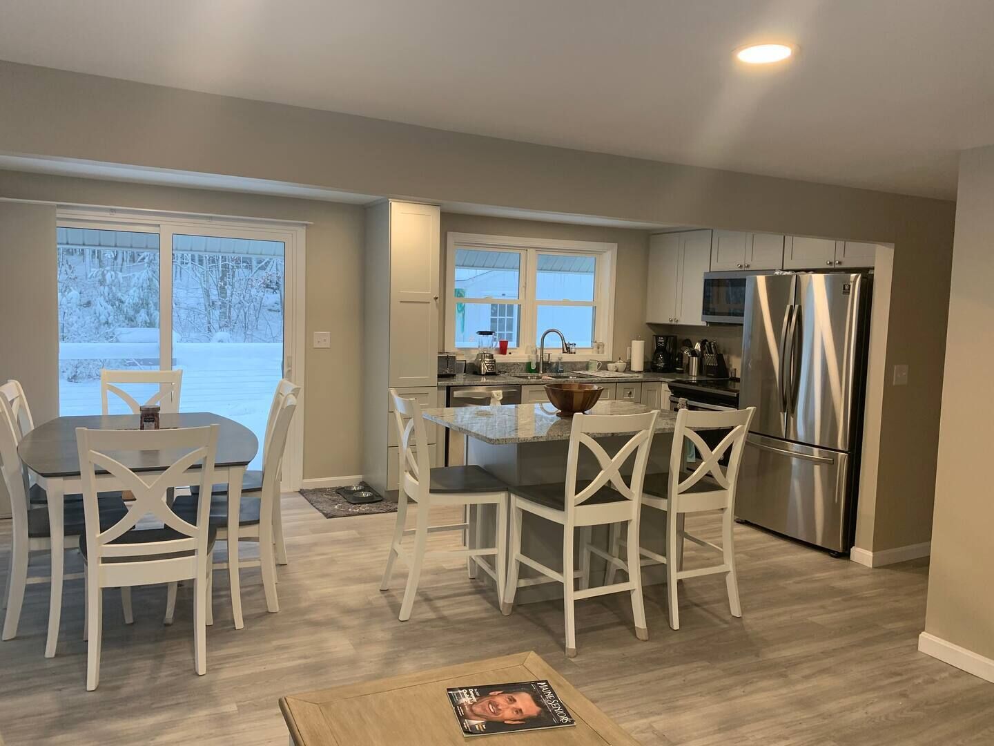 A modern kitchen with white cabinetry, a stainless steel refrigerator, and a dining area with white chairs.
