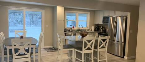 A modern kitchen with white cabinetry, a stainless steel refrigerator, and a dining area with white chairs.