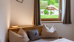 Une chambre à coucher avec une tête de lit en bois, une décoration en forme de cœur, une vue sur une maison par la fenêtre et un bol posé sur la table de chevet.