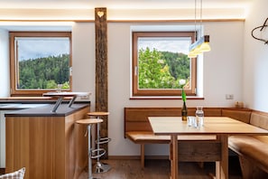 A modern kitchen with a wooden island, bar stools, and a bench seating area with a view of a forest.