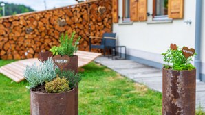 Un espace extérieur rustique agrémenté d’un mur en pierre, d’une terrasse en bois et de plantes en pot étiquetées « THYMIAN » et « PEARLSALL ».