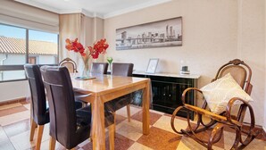 A dining area with a wooden table, black chairs, a wicker chair, a vase with red flowers, a framed picture on the wall, and a view of buildings outside. - Apartment 'La Bodegueta' with Private Terrace, Wi-Fi and Air Conditioning (Orba)